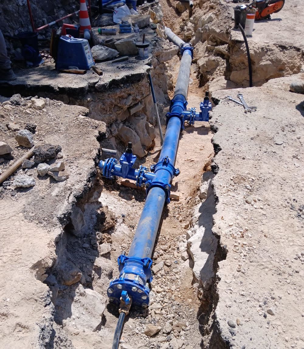 Conduite d'eau potable neuve posée en tranchée, robinets-vannes bleus, sur un chantier de travaux publics